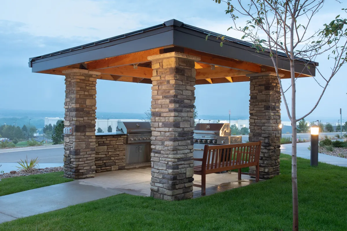 The image captures an inviting exterior scene with sturdy stone columns framing a well-appointed grilling area. Wooden benches and grill stations suggest opportunities for outdoor socializing, dining, and relaxation. The setting is welcoming and hints at shared experiences in the fresh air, suitable for guests looking to unwind after exploring the city.