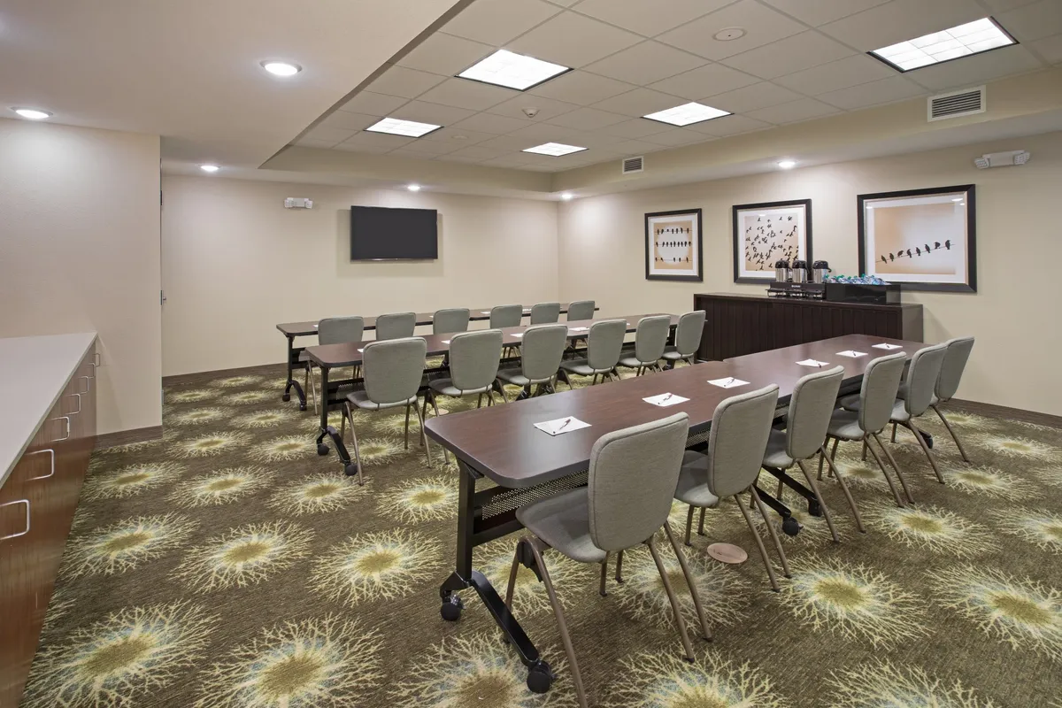 The image features a long conference table set for a business meeting, with modern artwork on the walls and a large presentation screen. The space is well-lit and organized, designed for productivity and collaboration.