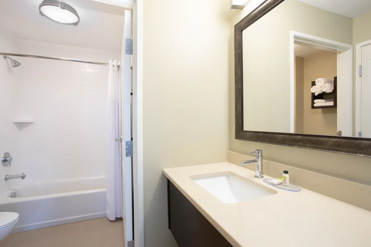 A modern, spacious bathroom equipped with a large mirror, sink, bathtub, and shelves neatly stacked with fresh towels. The room is bright and clean, creating an inviting atmosphere for self-care and relaxation.