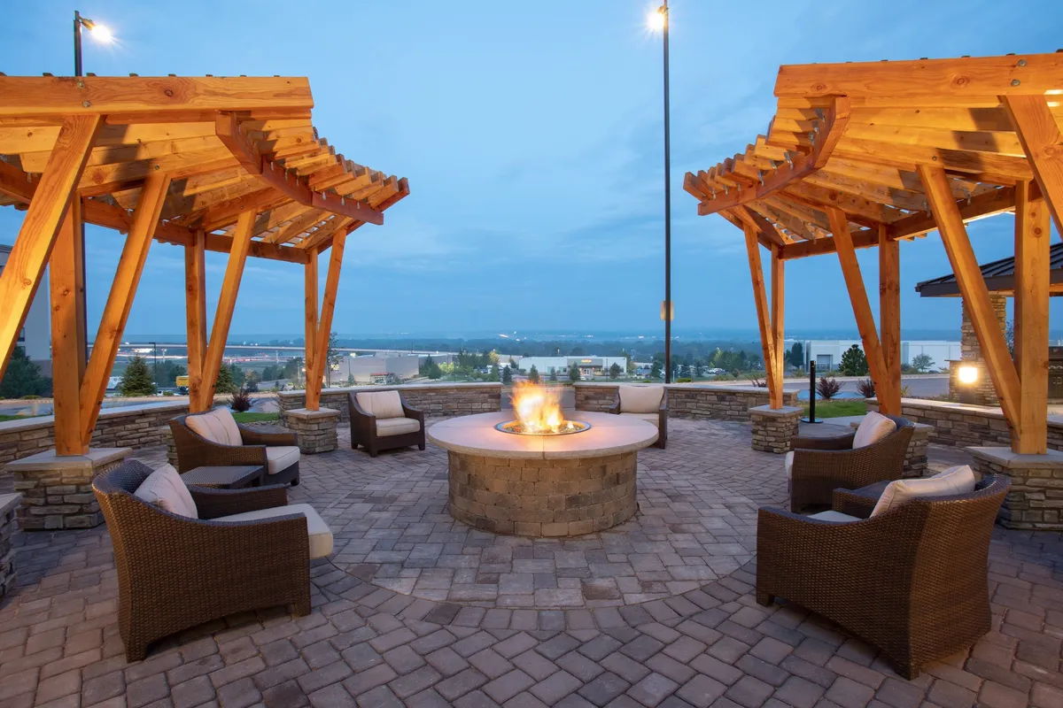 This image features a cozy outdoor communal area with a fire pit surrounded by wood pergolas and ample outdoor seating. The scene overlooks a landscaped view, evoking a sense of relaxation and social connection, ideal for unwinding after a productive day.