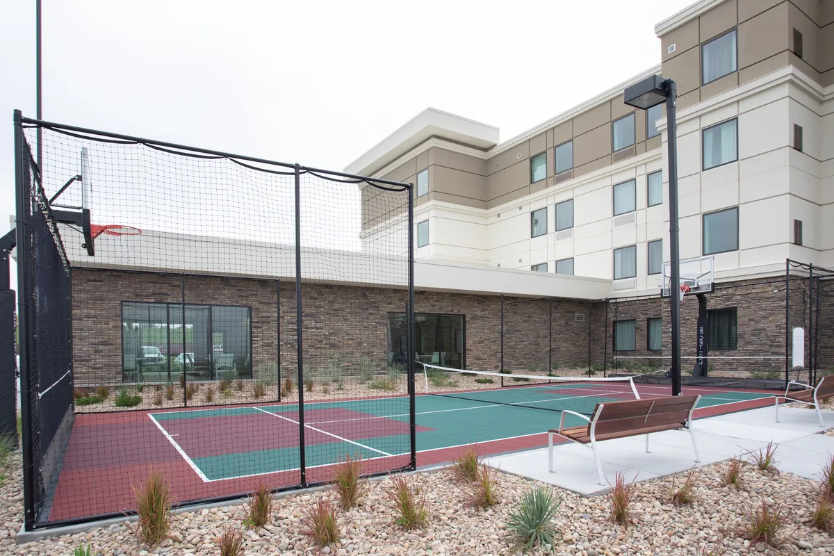 The image shows active recreation facilities outside the property, including a basketball hoop, tennis court, and benches for relaxation. The area is vibrant and well-maintained, offering guests the option to stay active and recharge in a communal setting.