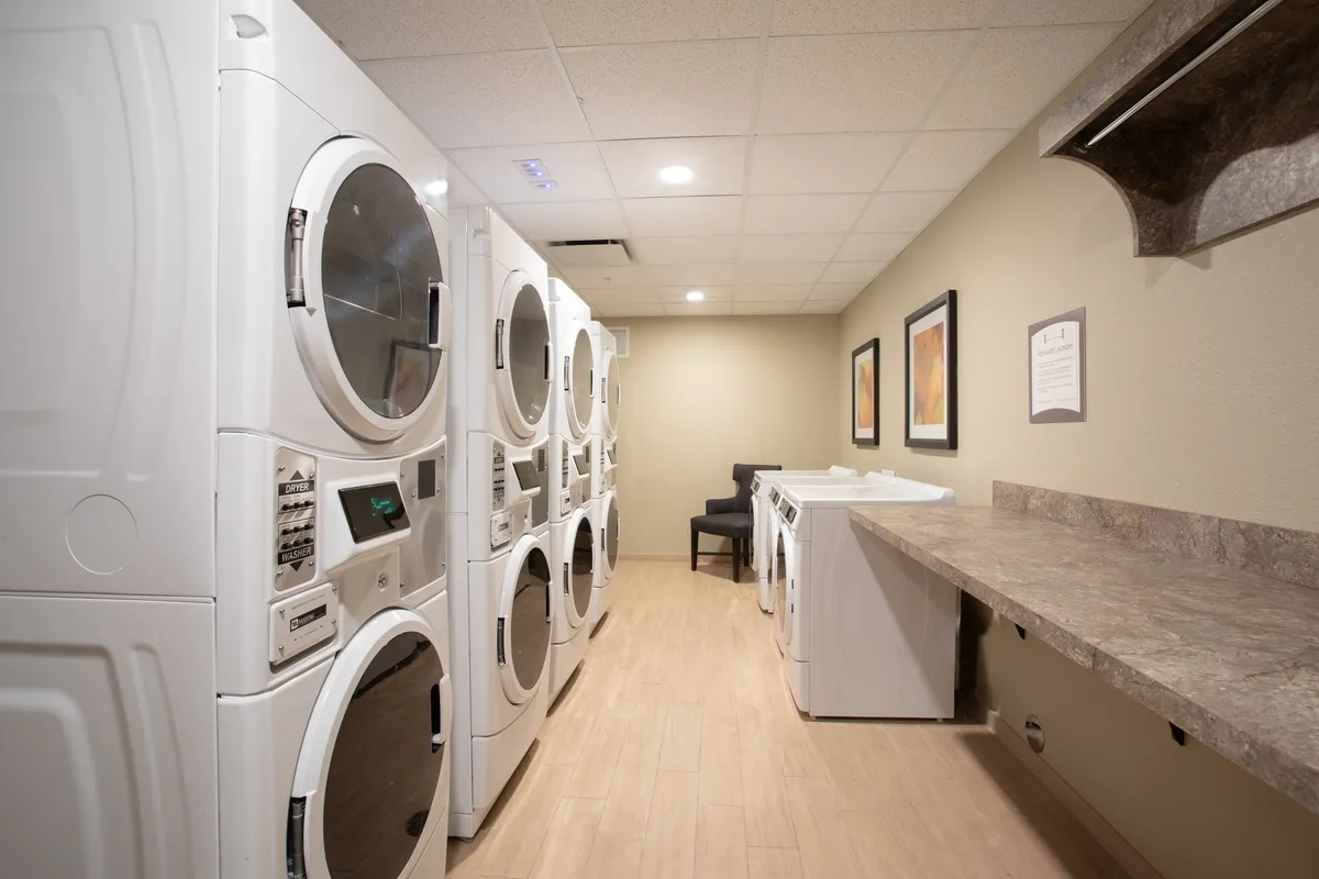 A practical interior space featuring modern laundry machines, a useful countertop, and a seating area where guests can wait comfortably or socialize. The area appears tidy and functional, reflecting the attention to guest needs and daily conveniences.