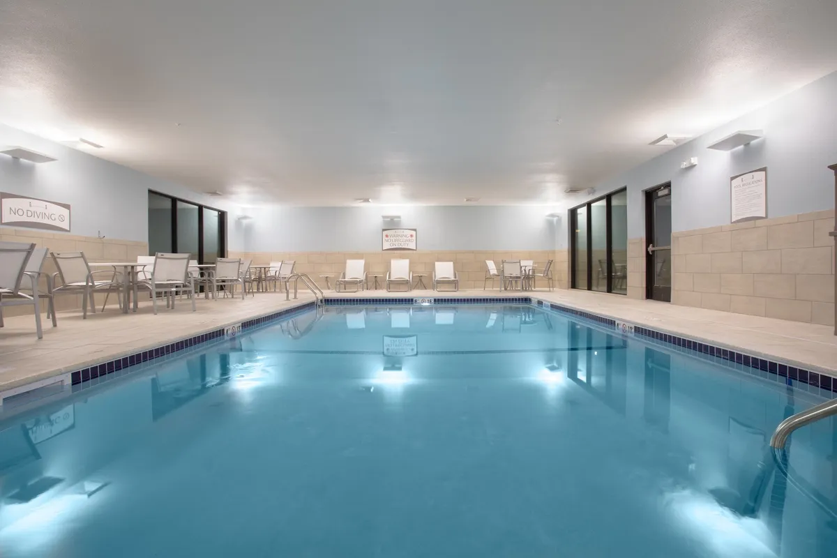 A serene indoor swimming pool with several lounge chairs lining the poolside and large glass doors letting in natural light. The tranquil setting makes it ideal for relaxing swims or socializing in a refreshing environment, regardless of the season.