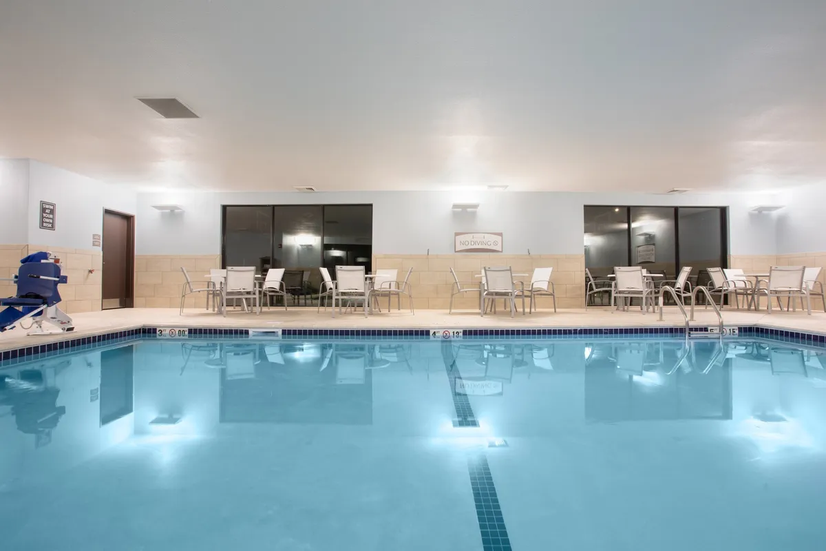 An indoor swimming pool is shown, surrounded by comfortable seating and accented with soft lighting. The atmosphere is tranquil, inviting guests to relax by the water after a day out. Poolside markings and open space make it suitable for both swimming and quiet moments with friends or solo relaxation.
